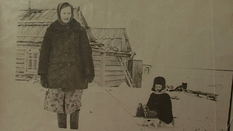 19. gadsimta 50. gadi Sibīrijā, pie koka būdiņas redzama sieviete, kas velk bērnu ragaviņās 
